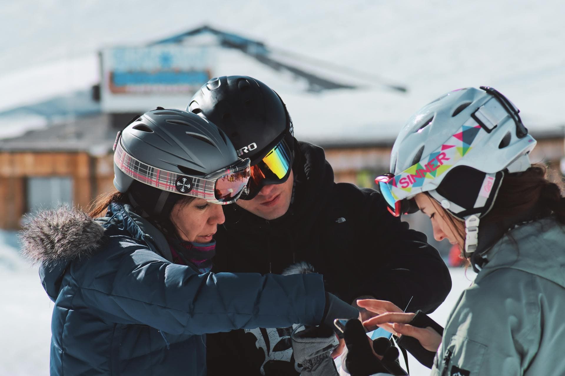 Three skiers in helmets checking a phone at the side of the slope