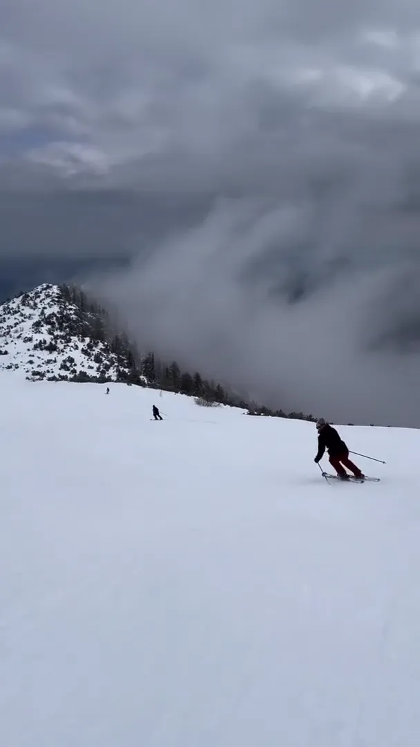 Skier in red carving across an open snowfield as cloud spills over the ridge behind