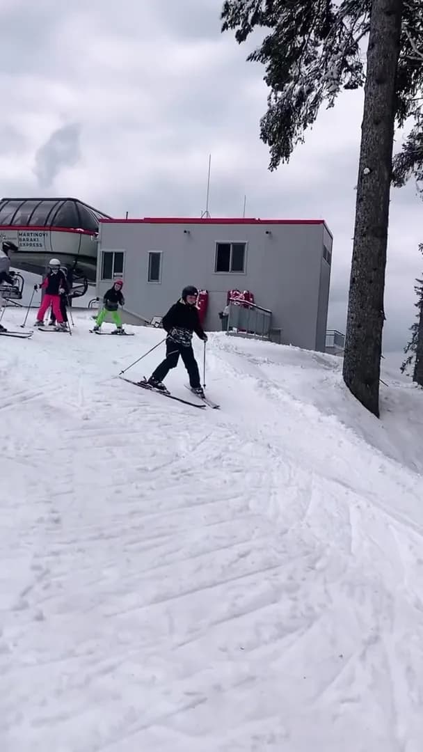 Skiers turning below the Martinovi Baraki Express lift station with a children's group behind
