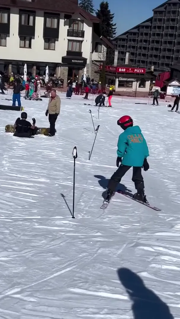 Child in a teal jacket skiing between training poles on the Borovets nursery slope
