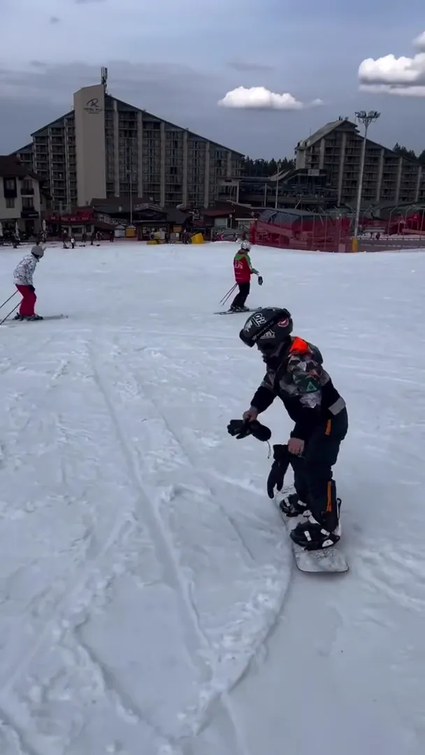 Young snowboarder strapping in at the Borovets base, hotels and lift station behind