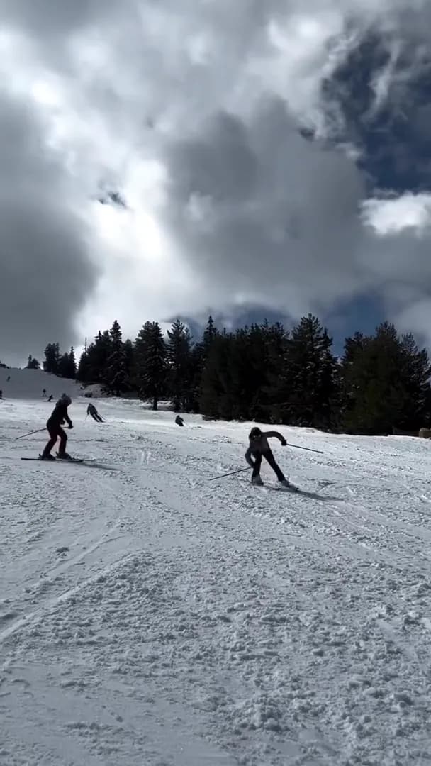 Two skiers turning on a sunlit piste as they are learning parallel skiing