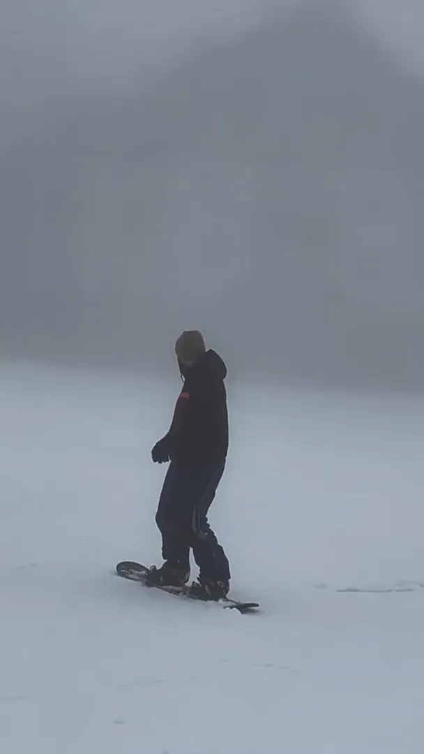 Lone snowboarder riding through thick fog in near-whiteout conditions