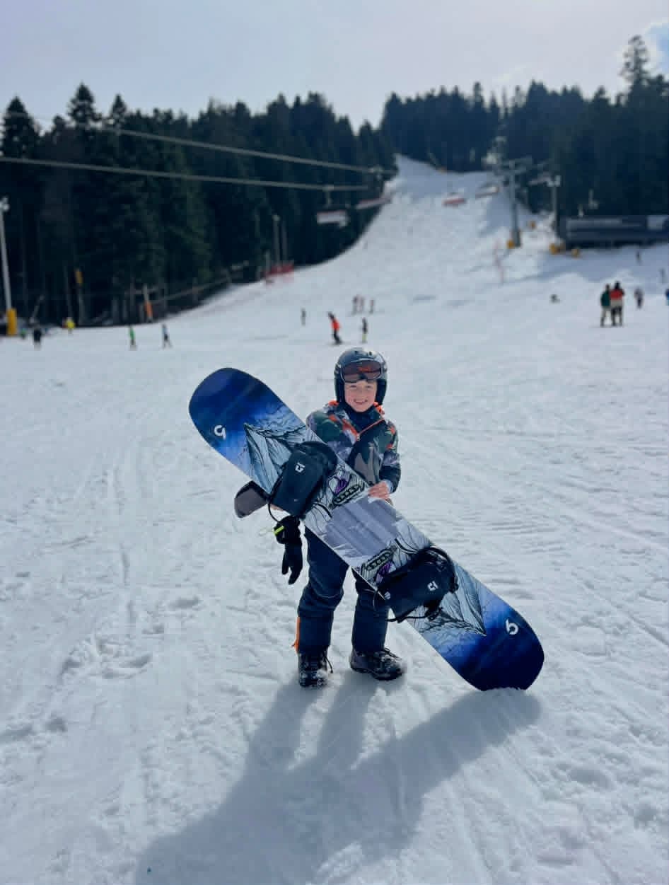 A small child carrying big snowboard